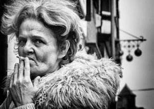 Street photography of an elderly woman smoking, captured in black and white.