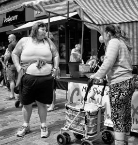 Street photography of a woman with a shopping cart depicted in black and white.
