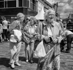 Black and white street photography of an older woman walking down a street.