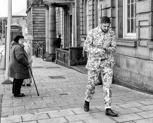 A man in a suit walking down the Huddersfield street.