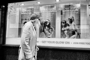 A man observing a poster in a store window in a street.