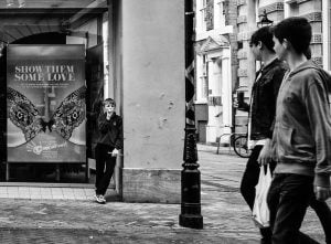 A street photography of a group of people standing on a sidewalk in front of a store.
