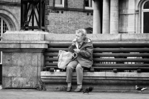 Street photography: An old woman surrounded by pigeons on a bench.