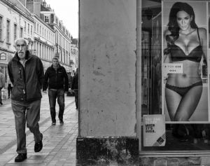 Street photography featuring a man walking down a street with a woman featured in a lingerie ad.