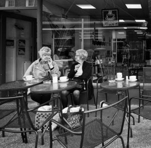 Street photography of two women at a table outside of a coffee shop.