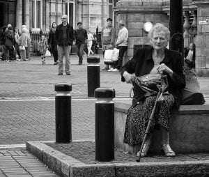 Street photography of a woman on a bench with a cane.