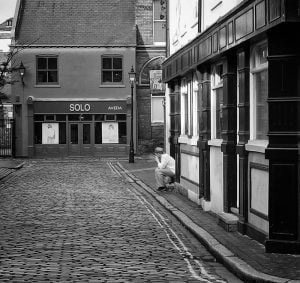 A monochrome street photograph featuring a cobblestone street.