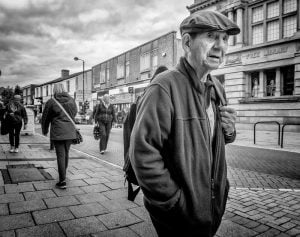 A black and white street photograph capturing an old man walking.