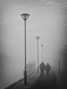 Street photography: Two people walking on a sidewalk in the fog.