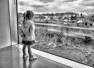 A little girl captured in street photography, gazing out a museum window.