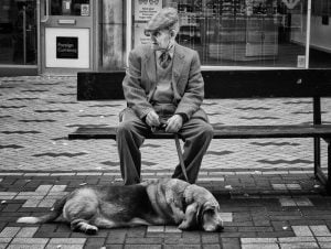 Street photography: an old man sitting on a bench with a dog.