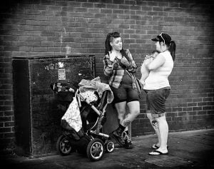Street photography of two women with a stroller in front of a brick wall.