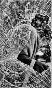 A monochrome photo of a figure peering through a shattered window along the coast.
