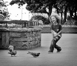 Black and white street photography of a boy playing with pigeons.