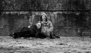 Black and white street photography capturing a homeless man sitting on the ground.