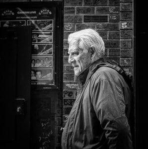 An elderly man captured in street photography with a brick wall backdrop.