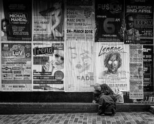 A street photography capturing a man sitting on a sidewalk in black and white.
