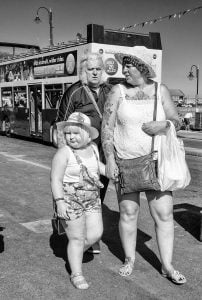 Street photography: Three women posing by a double decker bus.