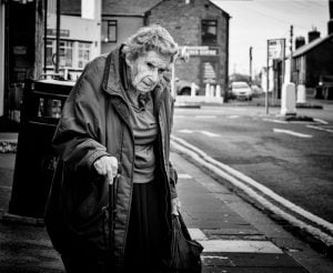 A street photography capturing an elderly woman strolling with a cane.