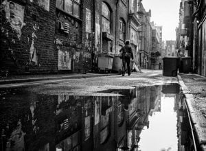 A monochrome street photography capturing a man strolling down an alley.