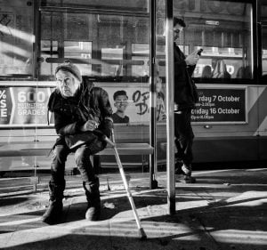 A woman captured in a street photography scene, sitting on a bench next to a bus.