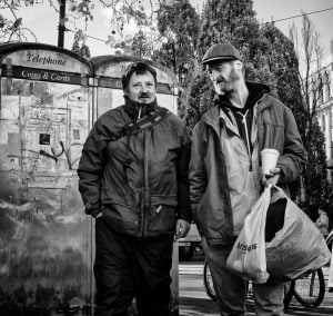 Street photography: Two men standing next to a public toilet.