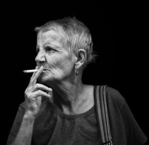 Street photography of an elderly woman smoking a cigarette captured in classic black and white.