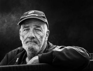 A street photography depicting a man in a baseball cap, captured in black and white.
