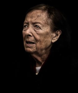 An old woman is looking at the camera in a dimly lit room during street photography.