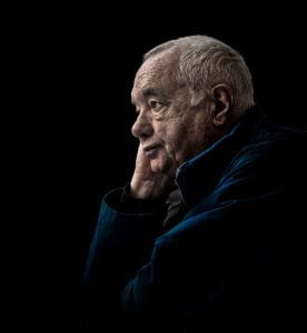 Street photography of an older man contemplating with his hand on his chin.