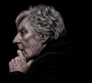 A street photography capturing an old woman deep in thought with her hand on her chin.