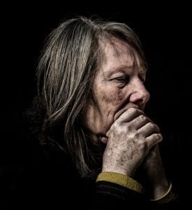 Street photography of an elderly woman lost in thought, chin in hand.