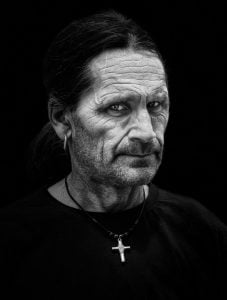 A street photography portrait of a man wearing a cross necklace.