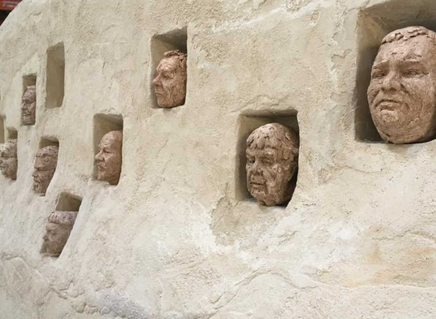 Street photography of a building's wall adorned with a array of intricately carved faces.