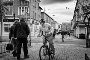 A street photography capturing a man riding a bike on a city street.
