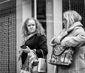 Street photography: Two women captivated by their phones in front of a store.