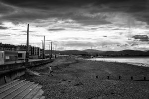 A black and white photo of a person walking on Rhyl beach.