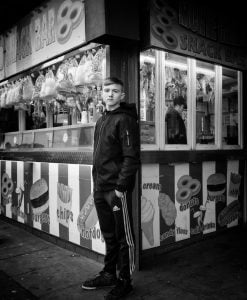 A black and white photo of a man standing in front of a food stand in Rhyl.
