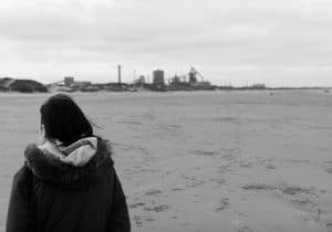 A monochrome street photograph featuring a woman strolling on the beach.