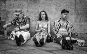 A street photography shot capturing a group of people sitting on the sidewalk in black and white.
