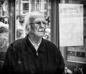 Street photography of an elderly man outside a shop window.