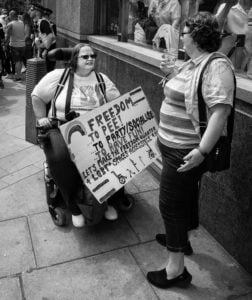 Street photography of a woman in a wheelchair holding a sign.